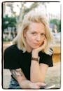 Portrait of a blonde woman resting on her hand outdoors, relaxed and thoughtful.