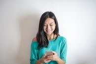 A happy woman in a green top smiling while using her smartphone indoors.